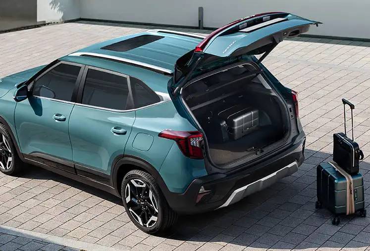The trunk of a 2026 Kia Seltos is open, with rolling suitcases propped up behind it on the brick floor