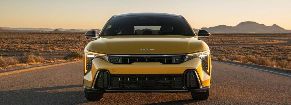 A yellow 2026 Kia K4 Hatchback faces the camera head on in front of a setting sun
