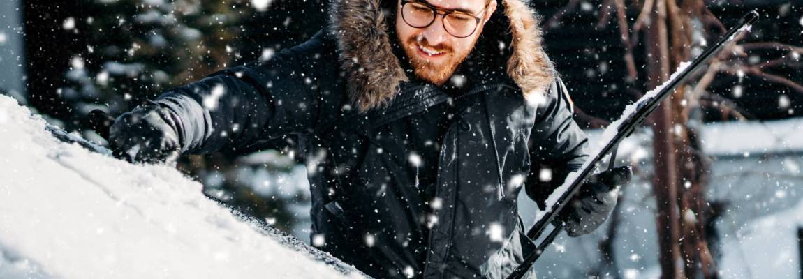 portrait of smiling man cleaning snow off his car during winter snowfall