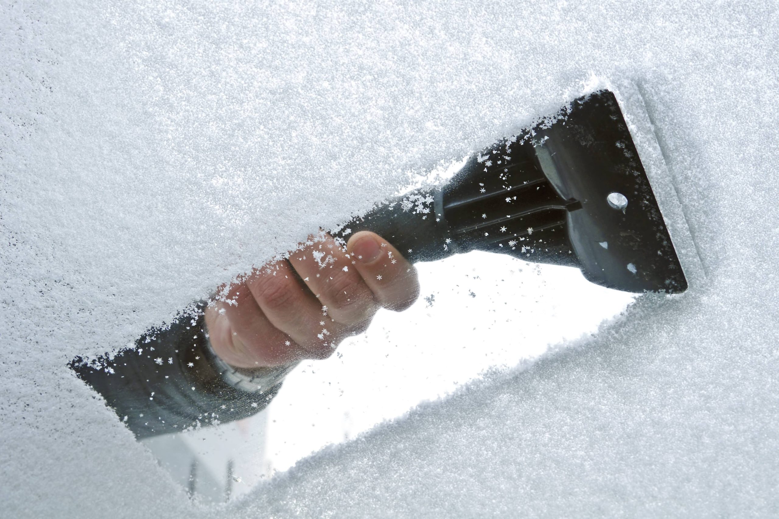 A hand scraping snow and ice from the car windscreen