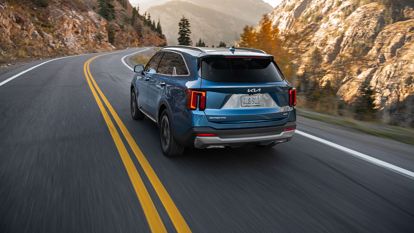 A blue 2026 Kia Sorento PHEV drives away from the camera down a mountain road
